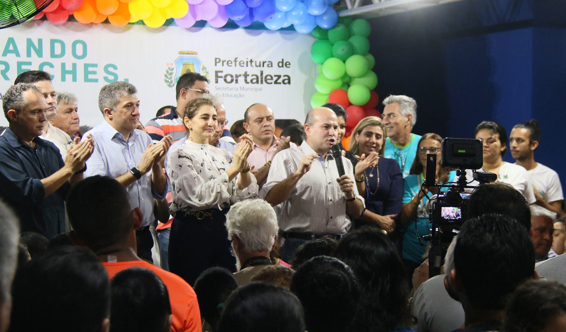prefeito roberto cláudio fala ao microfone num palco, rodeado de pessoas